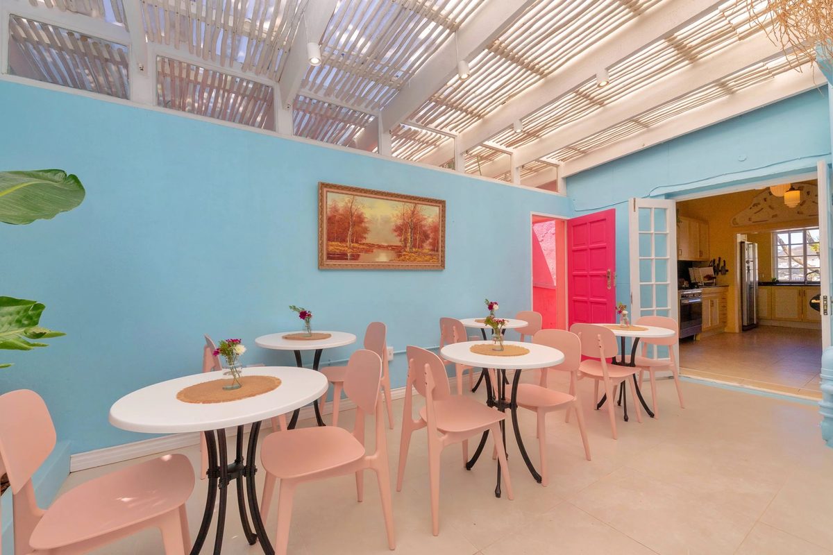 The breakfast area: pink chairs, round white tables and a pink door under a pergola