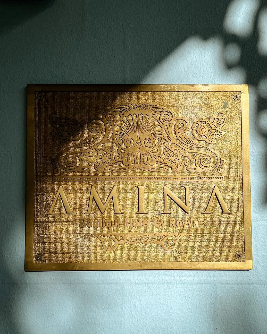 The brass AMINA plaque on the blue wall of the house